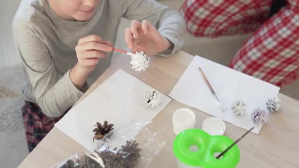 Mutter und Sohn dekorieren Fichtenzapfen mit weißer Farbe, um das Haus zu Weihnachten zu schmücken — Stockvideo
