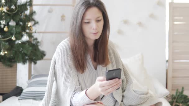 En kvinna drar ut ett kreditkort från sin väska på morgonen i sängen bredvid en dekorerad julgran — Stockvideo