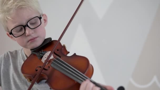 Seorang anak pirang dengan kacamata belajar untuk bermain biola. — Stok Video