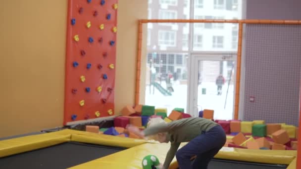 Beautiful boy blond jumps on a trampoline in a childrens playroom — Stock Video