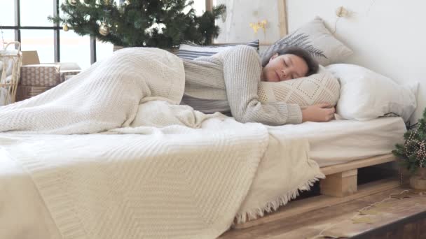 Egy gyönyörű nő felébred reggel az ágyban Karácsony reggel a karácsonyfa mellett. — Stock videók