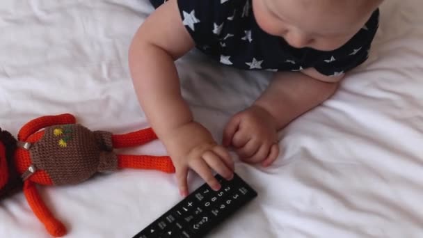 Een schattig jongetje speelt met de TV afstandsbediening thuis in zijn ouders bed — Stockvideo