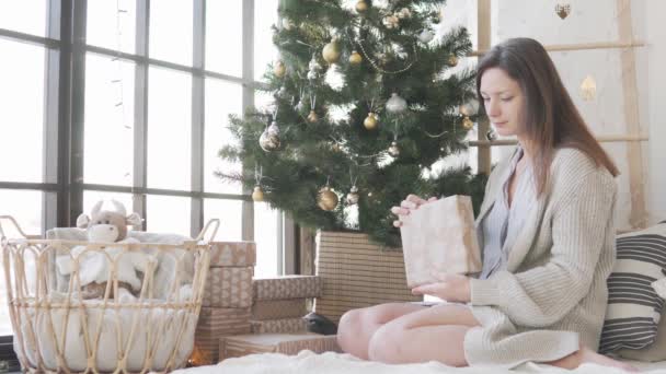 Een mooie vrouw opent een kerstcadeau thuis in bed — Stockvideo