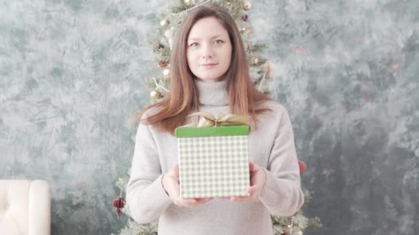 Una hermosa mujer estira una caja brillante con un regalo de Navidad hacia adelante a la cámara — Vídeo de stock