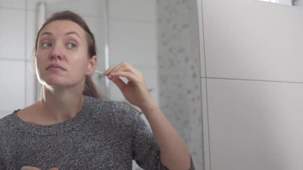 Una mujer se limpia las orejas con capullos de algodón por la mañana frente a un espejo — Vídeos de Stock