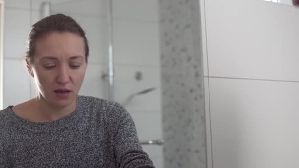 Женщина чихает и закрывает лицо руками дома в ванной, затем моет руки — стоковое видео