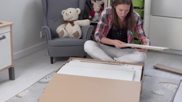 Μια όμορφη γυναίκα νοικοκυρά τραβά έξω από ένα μεγάλο κουτί με λεπτομέρειες για να συγκεντρώσει ένα τραπέζι στο παιδικό δωμάτιο — Αρχείο Βίντεο