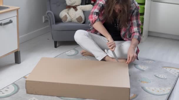 Женщина открывает большую картонную коробку с ножом — стоковое видео
