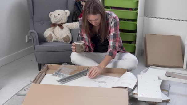 A beautiful woman drinks tea and collects a white table in the childrens room — Stock Video