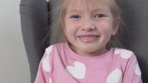 Маленькая девочка кокетливо улыбается в камеру и смотрит хитрыми глазами — стоковое видео