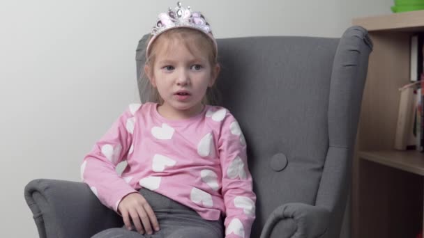 Забавная маленькая девочка сидит в детском кресле в короне и пижаме. — стоковое видео
