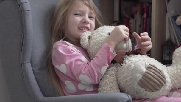 Roliga knull liten flicka leker med en nalle hemma i en barnstol — Stockvideo