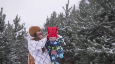 Karlı kışta parkta yürürken bir anne kucağında küçük bir çocuk taşır.