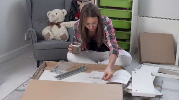 Женщина собирает мебель в детской комнате в соответствии с инструкциями дома — стоковое видео