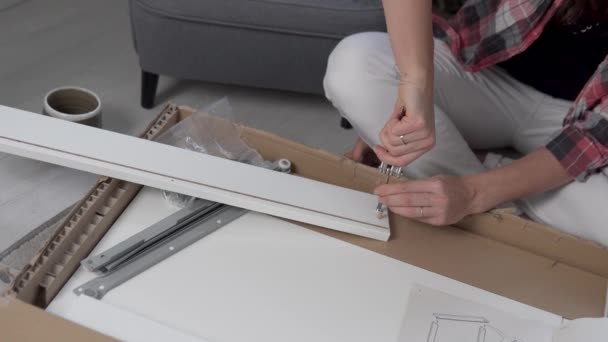 The woman twists the screw with a screwdriver into the detail from the furniture according to the instructions — Stock Video