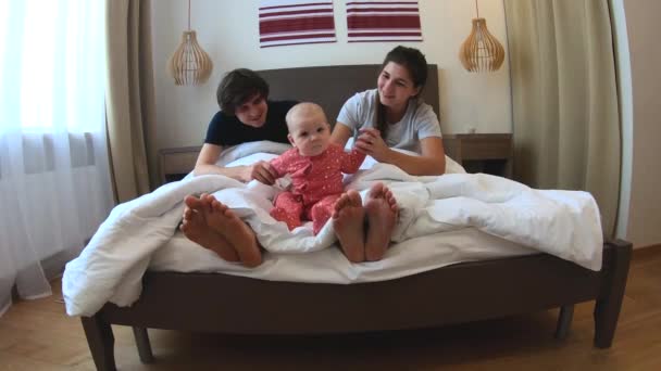 Um jovem casal se senta na cama com uma criança pequena — Vídeo de Stock