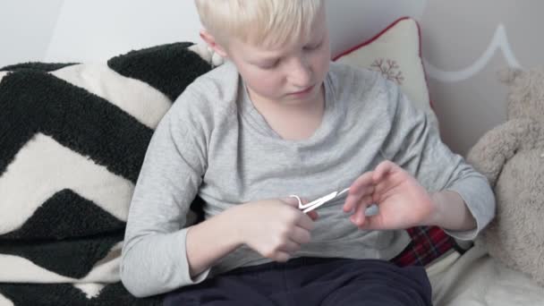 Lindo menino loiro corta suas unhas em suas mãos com tesoura — Vídeo de Stock