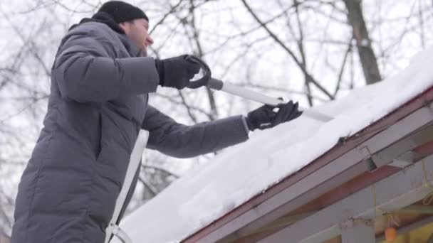 Ένας άντρας βγάζει ένα σωρό χιόνι από την οροφή με ένα φτυάρι. — Αρχείο Βίντεο