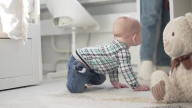 Küçük çocuk odada sürünüyor ve destekle ayağa kalkıyor.