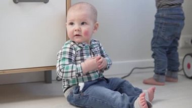 Küçük bir erkek bebek evde yerde oturuyor.