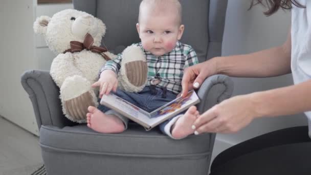 Moeder toont een boek met foto 's van een klein kind thuis in een kinderstoel — Stockvideo