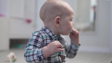 Küçük bir çocuk yerde oturuyor ve plastik bir oyuncağı yalıyor..