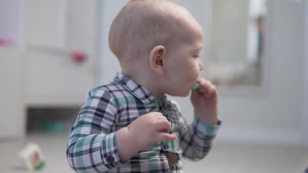 Un petit enfant s'assoit par terre et lèche un jouet en plastique. — Video