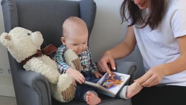 La tata legge il libro al bambino a casa e gli accarezza le gambe. — Video Stock