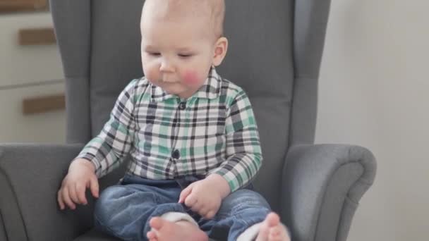 Un petit garçon mignon dans une chemise est assis dans un siège d'enfant à la maison — Video