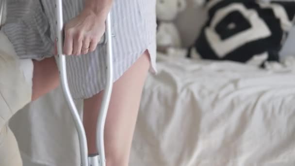 O femeie pe cârje în ipsos pe picior să se întindă pe pat acasă — Videoclip de stoc