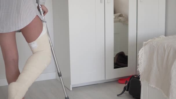 Kobieta ze złamaną nogą w gipsie porusza się po pokoju o kulach w domu. — Wideo stockowe