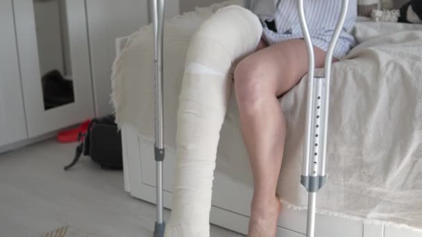 Μια γυναίκα μετά από χειρουργική επέμβαση στο πόδι της σε μια κατά μήκος και επιδέσμους παίρνει από το κρεβάτι σε πατερίτσες — Αρχείο Βίντεο