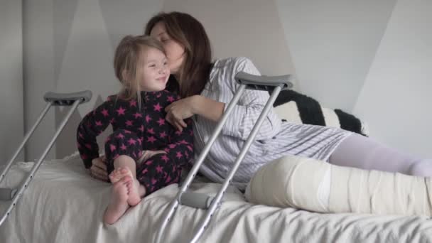 Маленькая девочка целует и обнимает свою мать со сломанной ногой — стоковое видео
