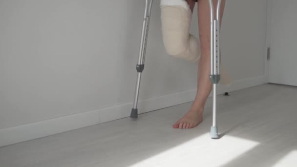 Bacağı kırık bir kadın hastane koğuşunda koltuk değnekleriyle yavaşça yürüyor.. — Stok video