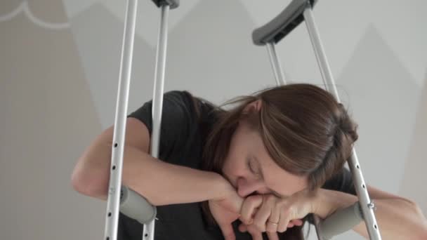 Una mujer triste se sienta apoyada en muletas. — Vídeos de Stock