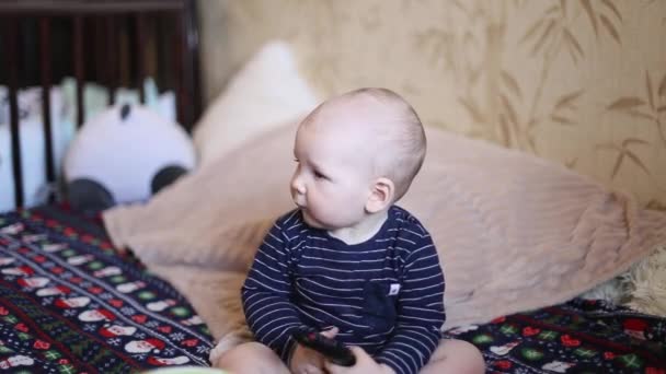 Un niño pequeño lame el televisor a distancia de la casa en la cama — Vídeo de stock