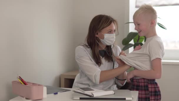 A female doctor listens to a stethoscope of a cheerful teenager boy — Stock Video