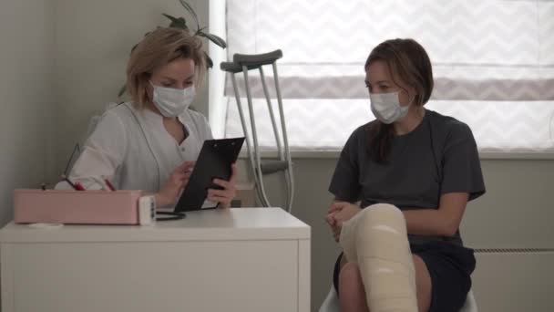 一位漂亮的女医生在病人的腿上做完手术后给她拿起拐杖 — 图库视频影像