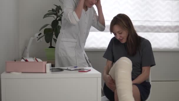 Uma mulher na consulta do hospital com um médico reabilitador depois de rasgar um tendão na perna — Vídeo de Stock