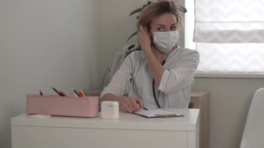 Kadın doktor masadan kalkar ve ofisten çıkar.