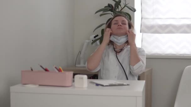 Yorgun bir kadın doktor hastanedeki ofisinden tıbbi bir maske çıkardı. — Stok video