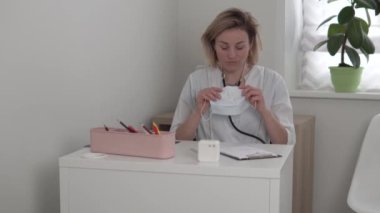 Kadın bir doktor yüzüne tıbbi maske takıp ofisten çıkıyor.