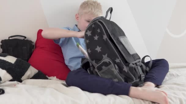 En pojke skolpojke kollar läroböcker i en skola ryggsäck hemma framför schoo — Stockvideo