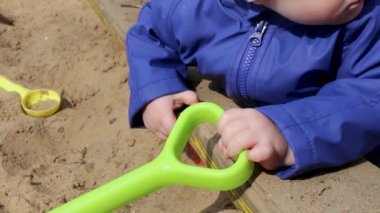 Yakından, kum havuzundaki küçük bir çocuğun ellerinde kürek.