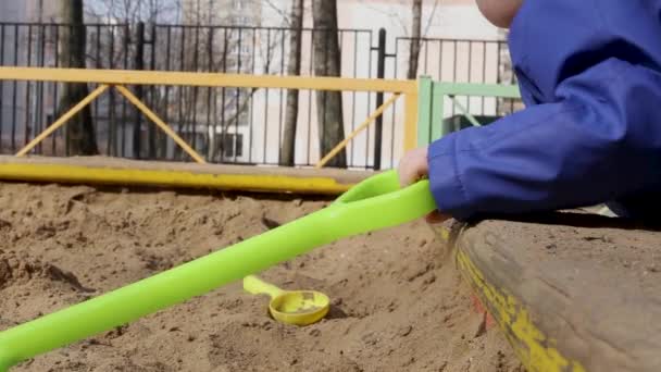 Маленький мальчик играет в песочнице на детской площадке весной — стоковое видео