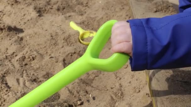 Рука ребенка держит лопату в песочнице на детской площадке весной — стоковое видео