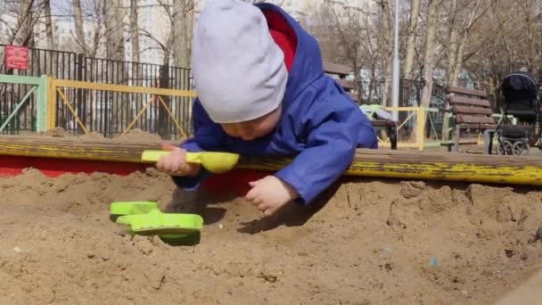 Un bambino carino gocciola sabbia in una sabbiera in primavera in Russia — Video Stock