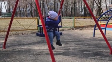 Küçük tatlı bir çocuk baharda parkta salıncakta sallanıyor.