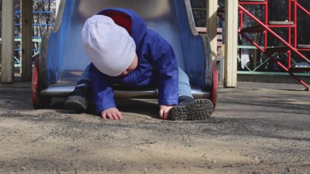 Uma criança pequena senta-se no fundo de uma colina no parque infantil — Vídeo de Stock