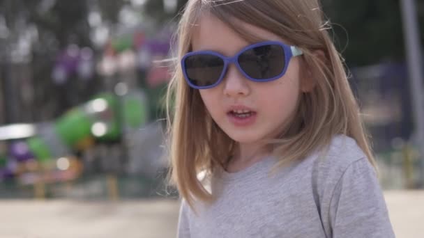 Ein kleines Mädchen mit Sonnenbrille und Erkältungssymptomen geht im Frühling nach draußen — Stockvideo